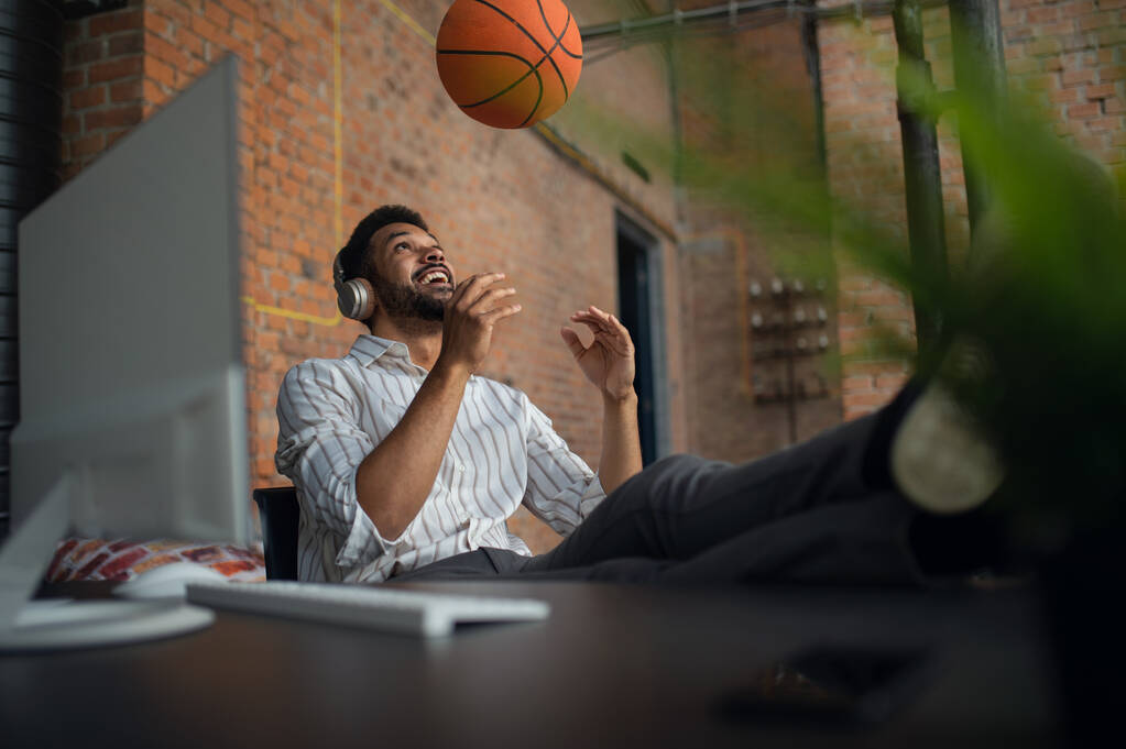 Χαρούμενος νεαρός επιχειρηματίας με ακουστικά και μπάλα κάνει διάλειμμα στο γραφείο, ξεκουράζεται. - Φωτογραφία, εικόνα