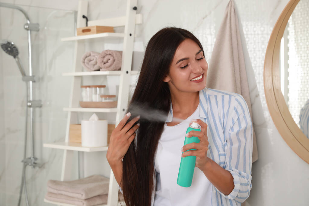 Woman applying dry shampoo onto her hair in bathroom - Photo, Image