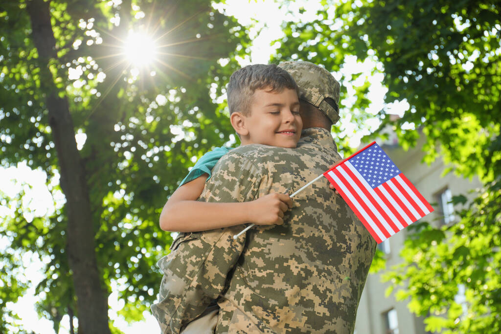Asker ve küçük oğlu Amerika bayrağıyla dışarıda kucaklaşıyorlar. - Fotoğraf, Görsel