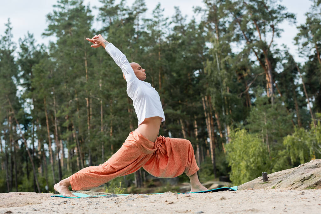 вид збоку буддиста, який практикує йогу в позі воїна з піднятими руками в лісі
 - Фото, зображення