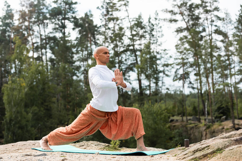 buddhist en pantalones harem practicando yoga en pose guerrera al aire libre - Foto, Imagen