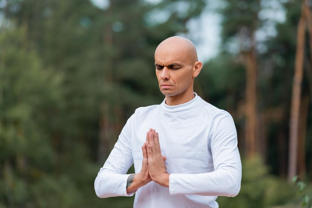 buddysta w bluzie modlący się z zamkniętymi oczami na zewnątrz - Zdjęcie, obraz