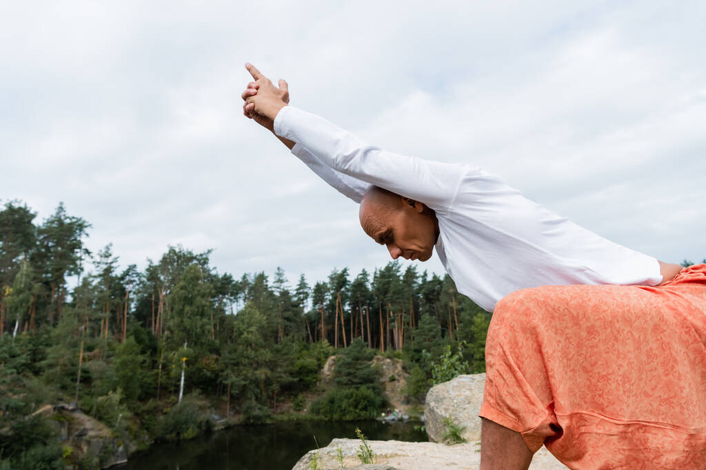 Buddhist im weißen Sweatshirt meditiert in Yoga-Pose mit erhobenen Händen im Freien - Foto, Bild