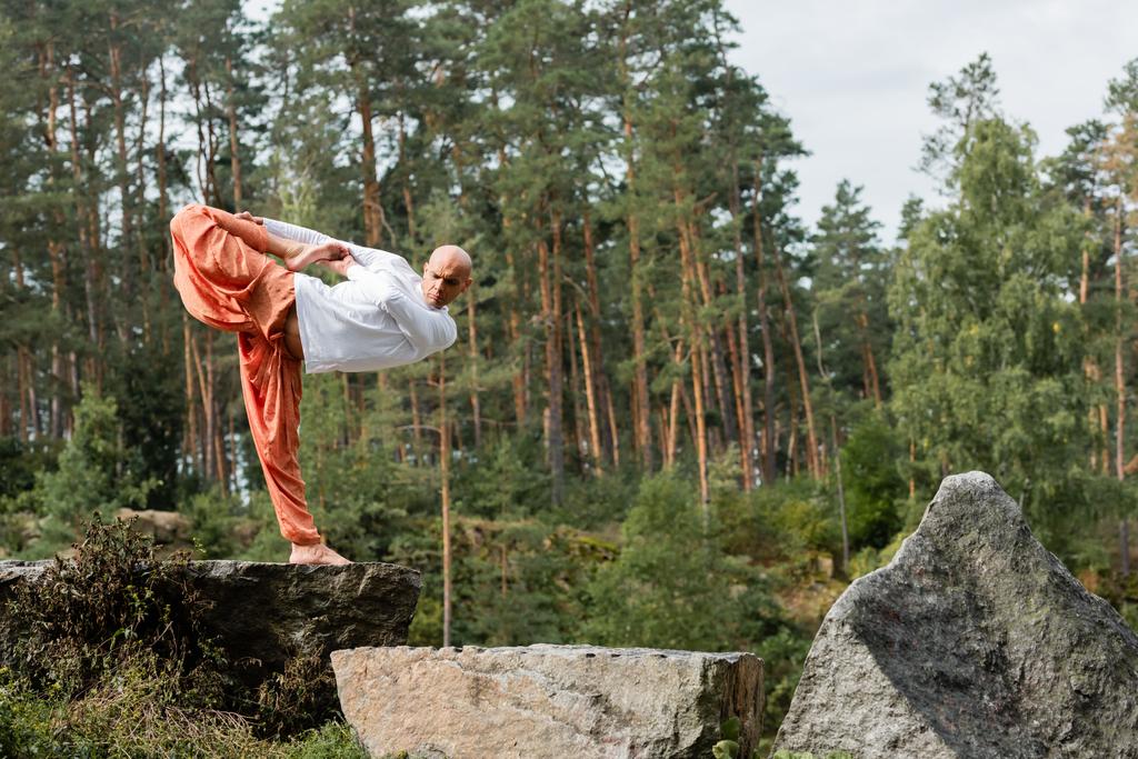 budista descalzo practicando yoga en media luna posan sobre rocas en bosque - Foto, Imagen