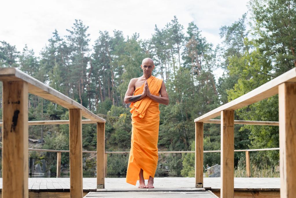 vista completa del monje budista rezando en plataforma de madera en el bosque - Foto, Imagen