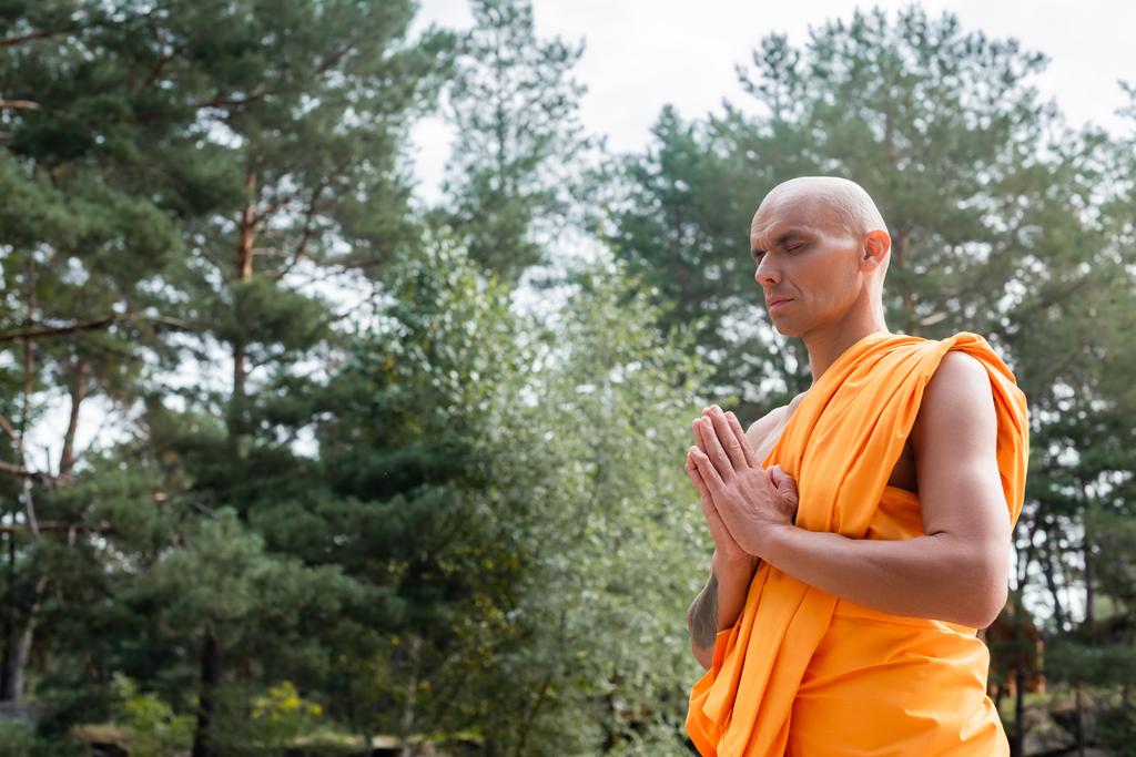 buddysta w pomarańczowej szacie modlący się z zamkniętymi oczami na zewnątrz - Zdjęcie, obraz