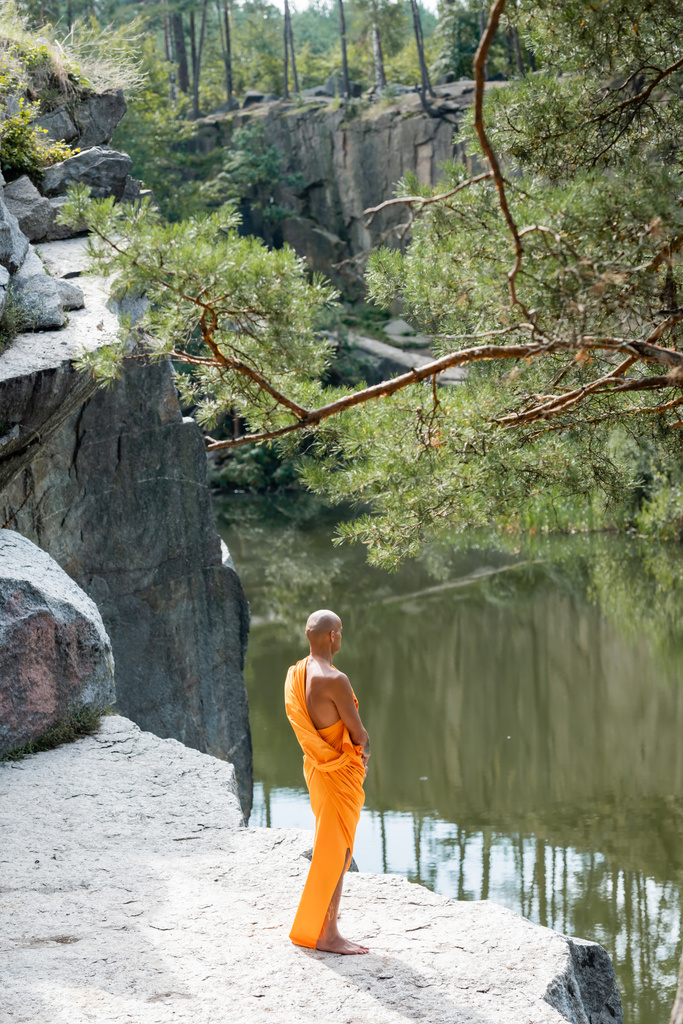 wysoki kąt widzenia buddystów w pomarańczowym kasaja medytujących na skalistym klifie nad wodą - Zdjęcie, obraz