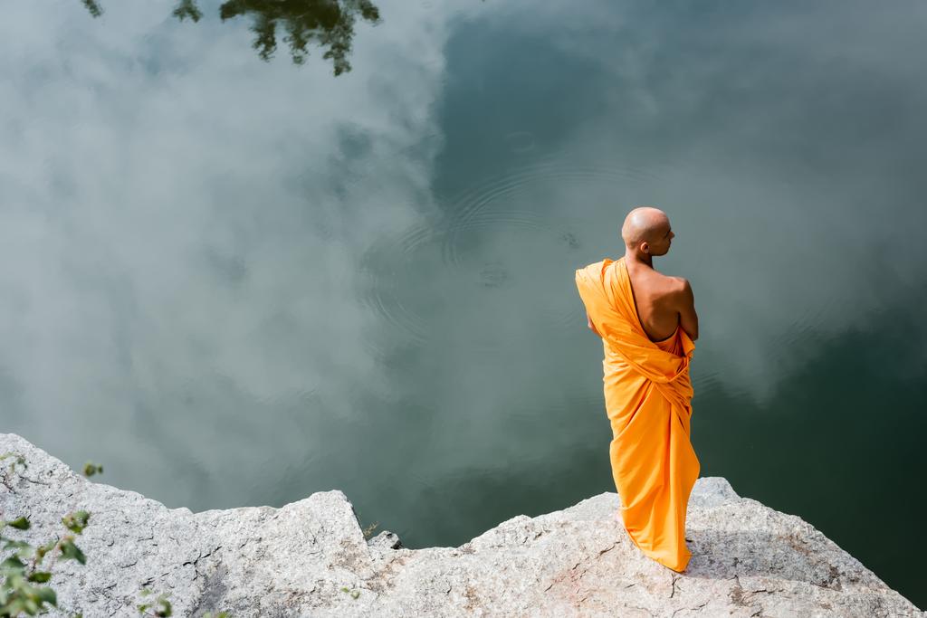 vysoký úhel pohledu buddhistického mnicha meditujícího na skalnatém útesu nad vodou - Fotografie, Obrázek