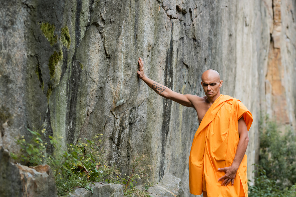 buddhist σε πορτοκαλί kasaya αγγίζοντας βράχο, ενώ διαλογίζεται με κλειστά μάτια - Φωτογραφία, εικόνα