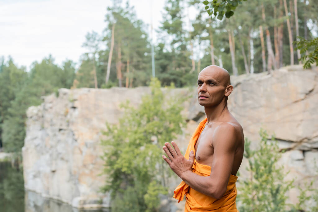 Buddhist schaut weg, während er mit betenden Händen im Freien meditiert - Foto, Bild
