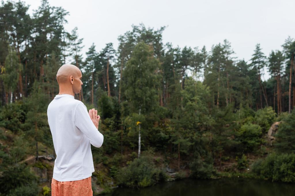 buddysta w białej bluzie modlący się nad jeziorem w lesie - Zdjęcie, obraz