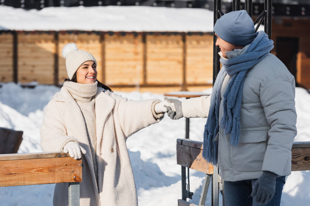 uśmiechnięta młoda para w czapkach zimowych patrząc na siebie trzymając się za ręce na zewnątrz - Zdjęcie, obraz