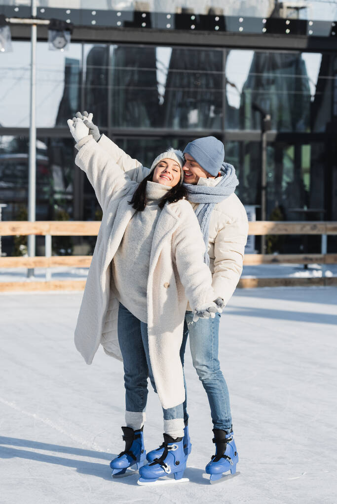 comprimento total de feliz jovem e mulher em chapéus de inverno patinação na pista de gelo - Foto, Imagem