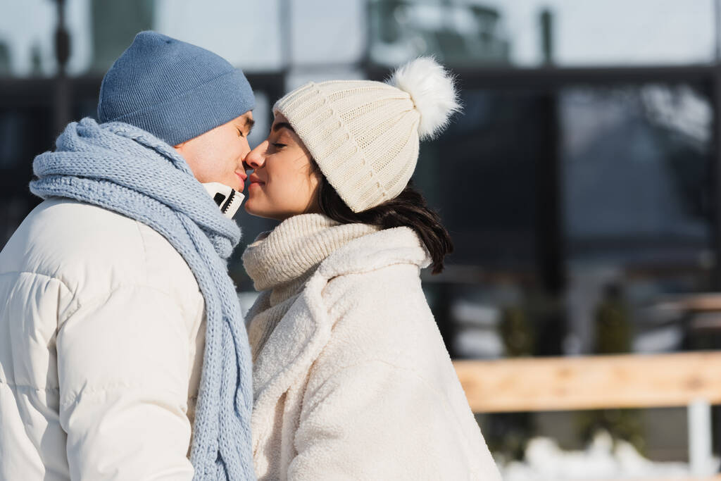 νεαρό ζευγάρι με χειμωνιάτικα καπέλα φιλιούνται έξω  - Φωτογραφία, εικόνα
