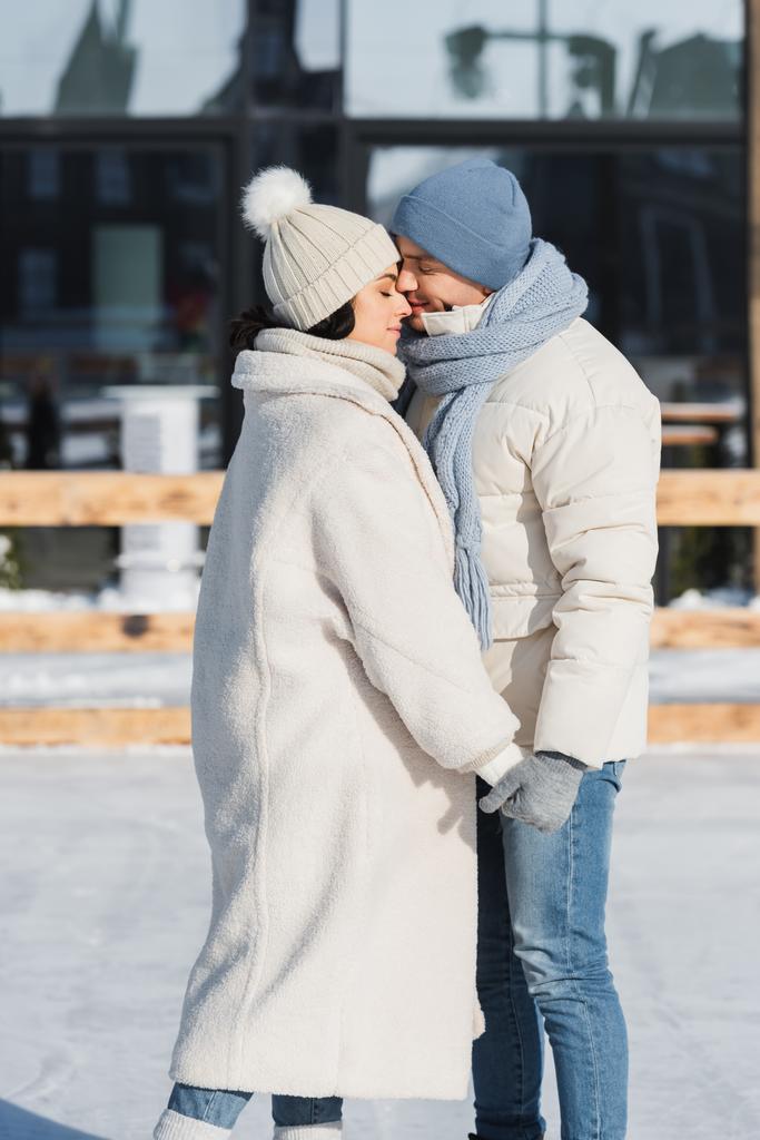 Kışlık şapkalı genç çift dışarıda öpüşürken el ele tutuşuyorlar.  - Fotoğraf, Görsel