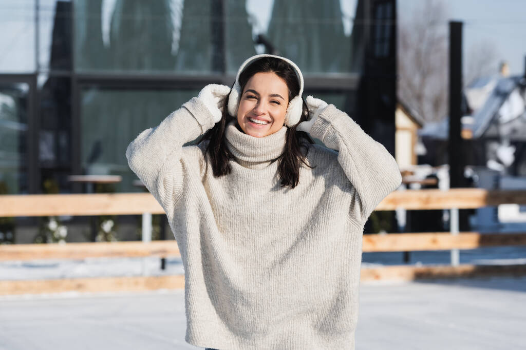 ウインタータイムのセーターと耳のマフを着た陽気な若い女性 - 写真・画像