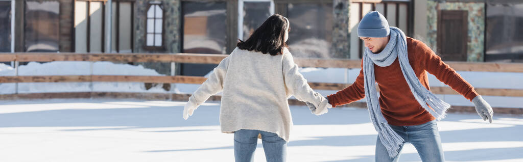 jeune femme dans des cache-oreilles tenant la main avec petit ami sur la patinoire, bannière - Photo, image