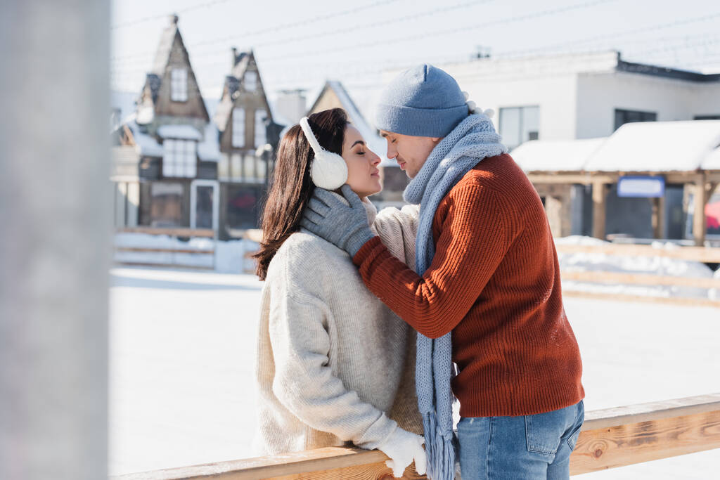 vue latérale d'un couple embrassant près d'une bordure en bois sur une patinoire  - Photo, image