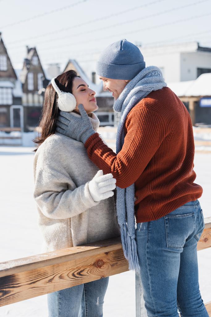 氷の上の木製の境界線の近くでキスをする陽気なカップルの側面図  - 写真・画像