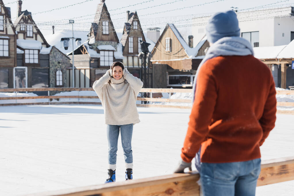 jeune femme souriante en patins à glace regardant son petit ami flou au premier plan - Photo, image