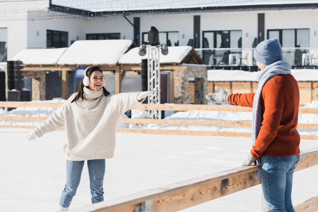 jeune femme souriante en patins à glace patinant avec la main tendue près du petit ami  - Photo, image