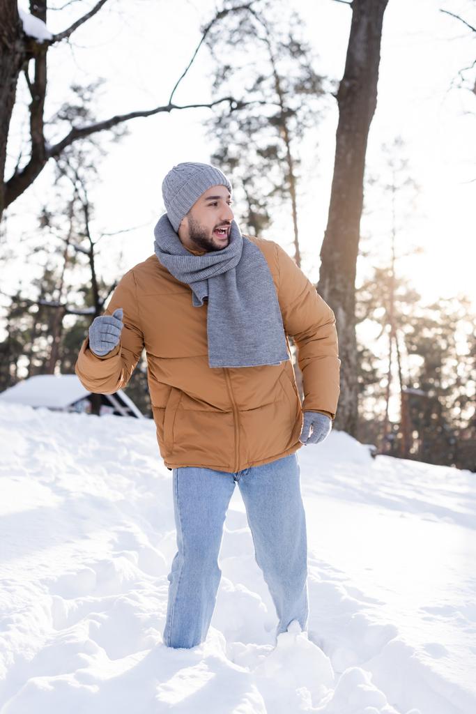 Positieve man met hoed en sjaal kijken weg in de sneeuw buiten  - Foto, afbeelding