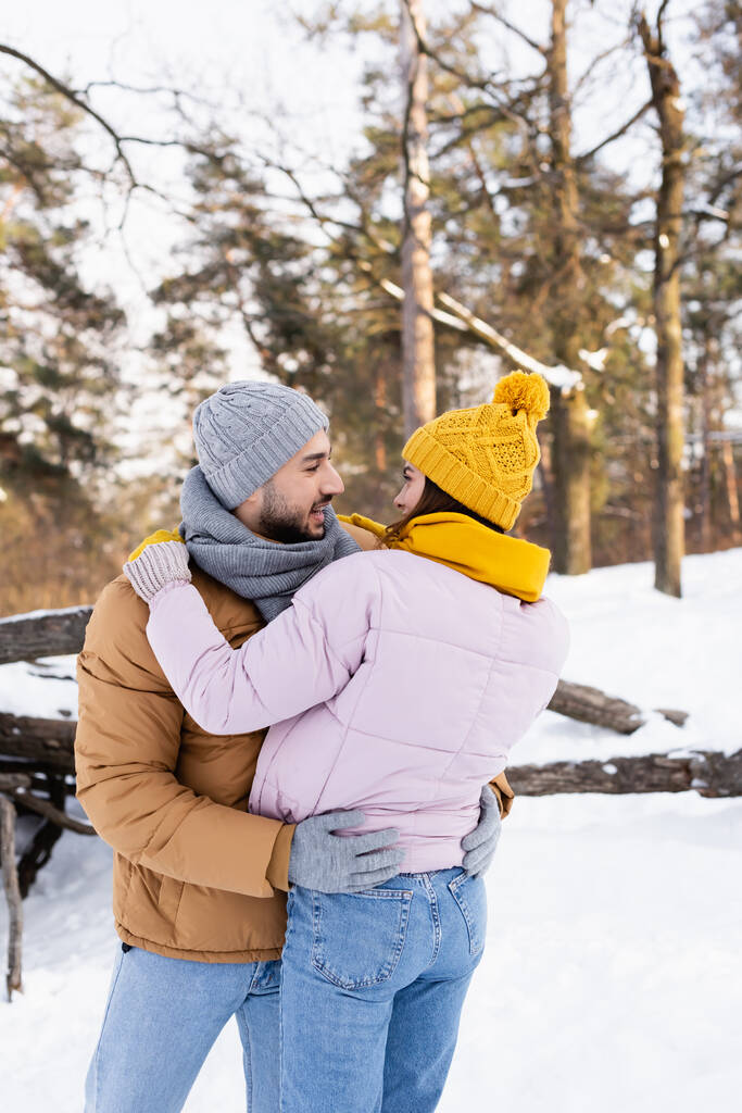 Boční pohled na šťastný pár objímání a při pohledu na sebe v zimním parku  - Fotografie, Obrázek
