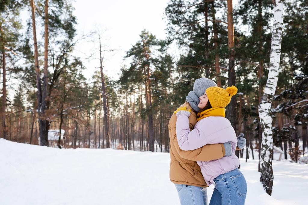 Πλευρική άποψη της γυναίκας χαμογελώντας και αγκαλιάζοντας φίλο στο πάρκο το χειμώνα  - Φωτογραφία, εικόνα