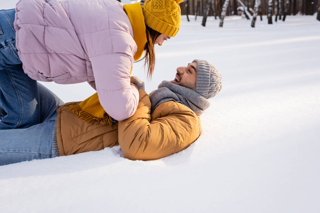 Вид сбоку веселой пары, играющей на снегу в парке  - Фото, изображение