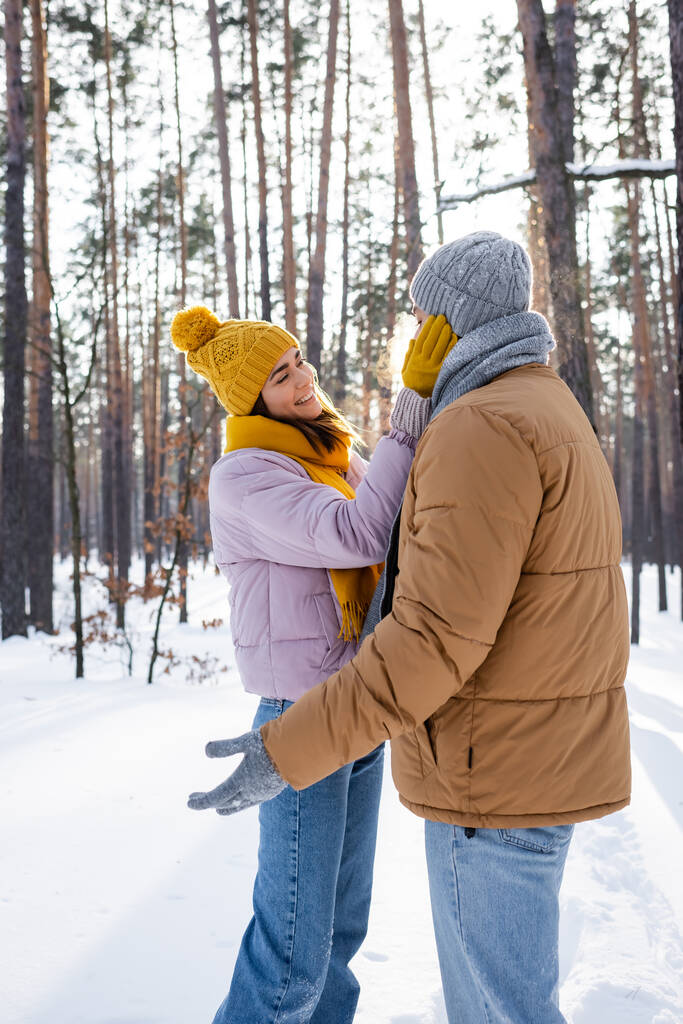 ładna kobieta uśmiecha się dotykając twarzy chłopaka w zimowym parku  - Zdjęcie, obraz