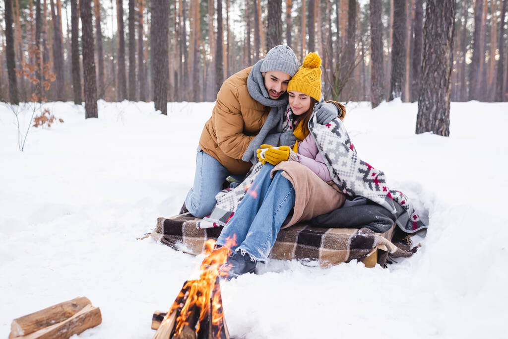 Muž objímání přítelkyně s pohárem v blízkosti táboráku v zimním parku  - Fotografie, Obrázek