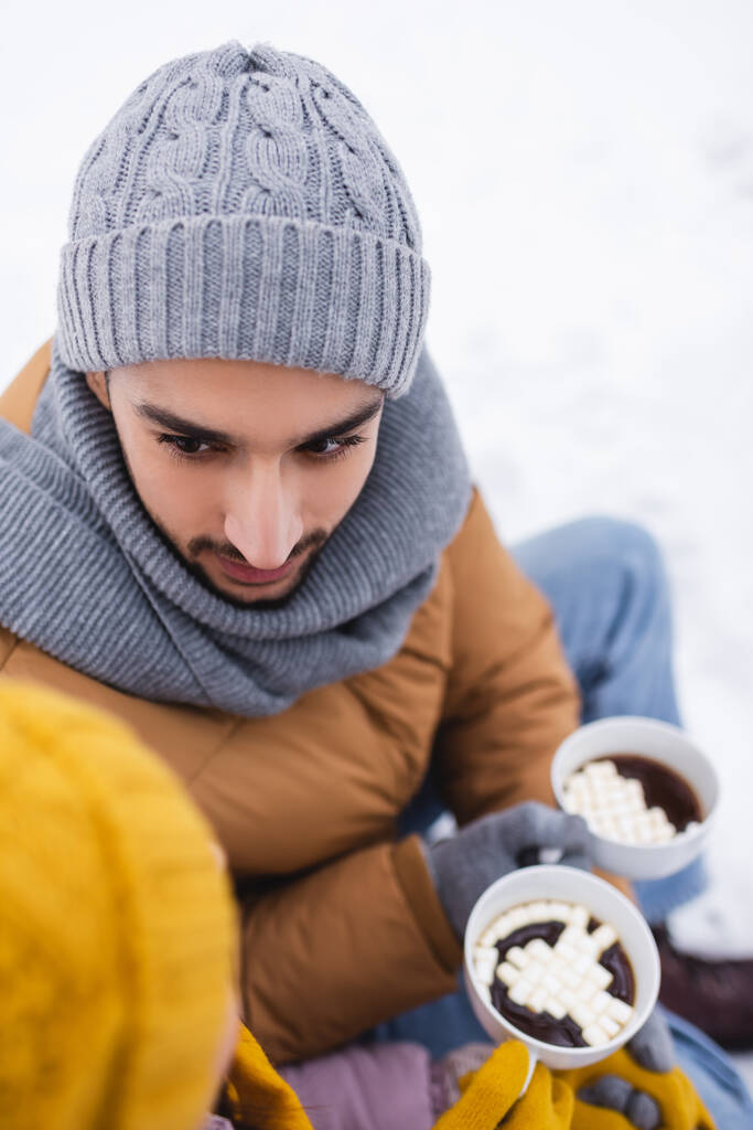 Vista aerea dell'uomo che guarda la fidanzata mentre tiene una tazza di cacao nel parco invernale  - Foto, immagini