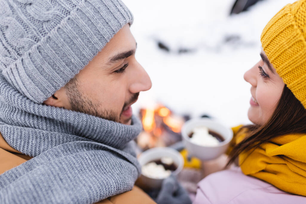 Casal sorridente em chapéus de malha olhando um para o outro no parque de inverno  - Foto, Imagem