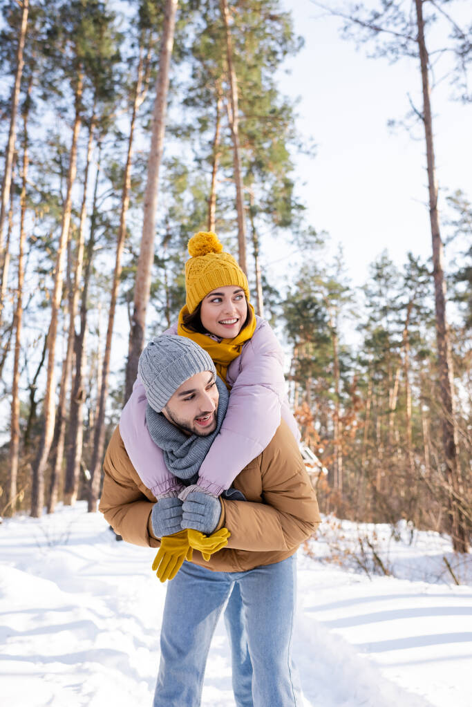 Χαρούμενη γυναίκα που αγκαλιάζει το αγόρι της και κοιτάζει αλλού στο χειμερινό πάρκο  - Φωτογραφία, εικόνα