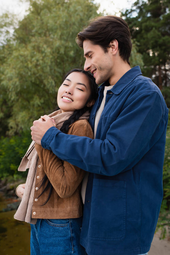 Hombre abrazando asiático novia al aire libre durante fin de semana  - Foto, Imagen