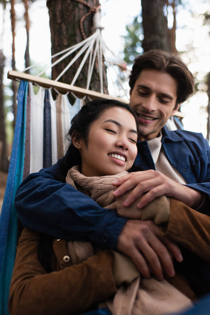 Uomo offuscata abbracciando ragazza asiatica in amaca in autunno  - Foto, immagini