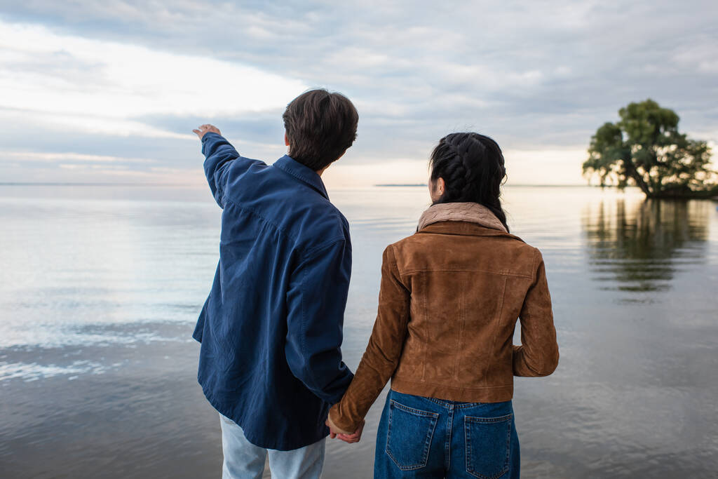 Visão traseira do casal de mãos dadas e homem apontando para o mar - Foto, Imagem