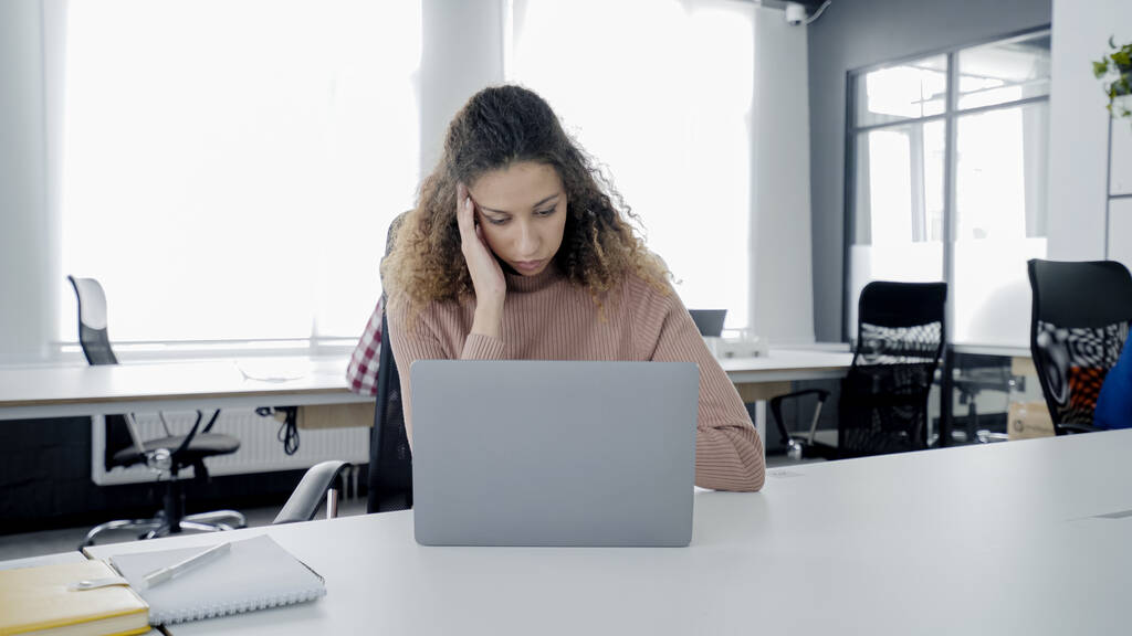 Mujer joven que tiene dolor de cabeza en el lugar de trabajo, trabajando en el ordenador portátil en la oficina, no se siente bien - Foto, imagen