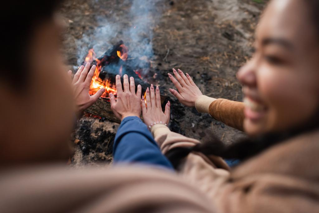 wazig paar verwarmende handen in de buurt van kampvuur tijdens het weekend  - Foto, afbeelding