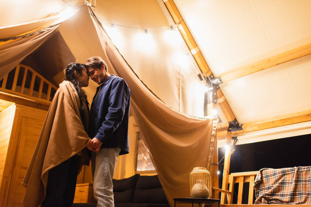 Счастливая межрасовая пара, держащаяся за руки на гламурной террасе дома вечером  - Фото, изображение