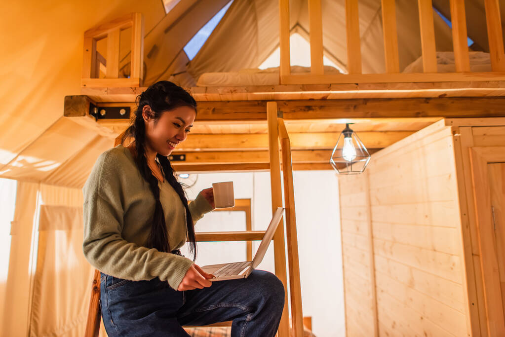Smiling asian woman holding laptop in glamping house  - Photo, Image