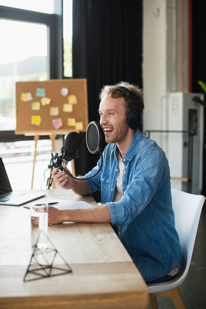θετικός ραδιοφωνικός ξενιστής σε ακουστικά που γελάει στο στούντιο  - Φωτογραφία, εικόνα