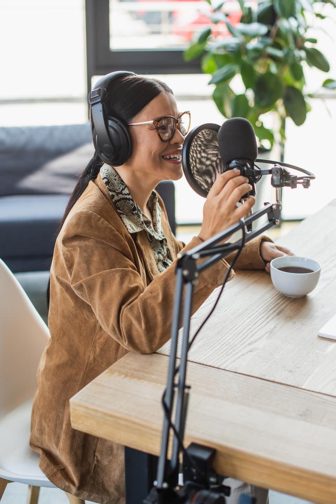 alegre asiático rádio host em óculos e fones de ouvido falando durante podcast - Foto, Imagem