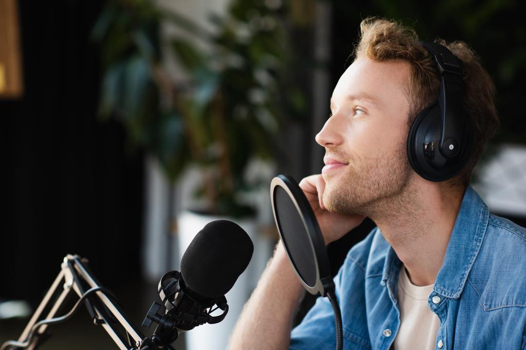 positive radio host in headphones looking away in podcast studio  - Photo, Image