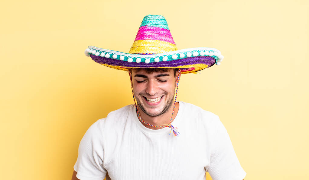 Młody przystojniak śmiejący się na głos z jakiegoś śmiesznego żartu. meksykańska koncepcja kapelusza - Zdjęcie, obraz