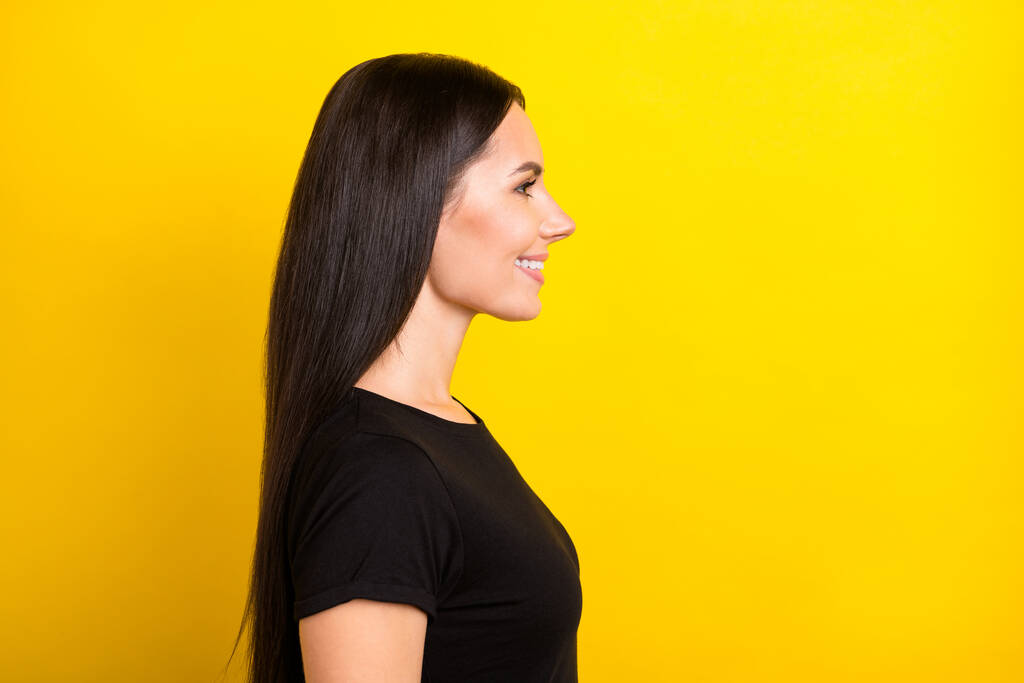 Profiel foto van positieve dame stralende glimlach kijken lege ruimte dragen zwarte t-shirt geïsoleerde gele kleur achtergrond - Foto, afbeelding