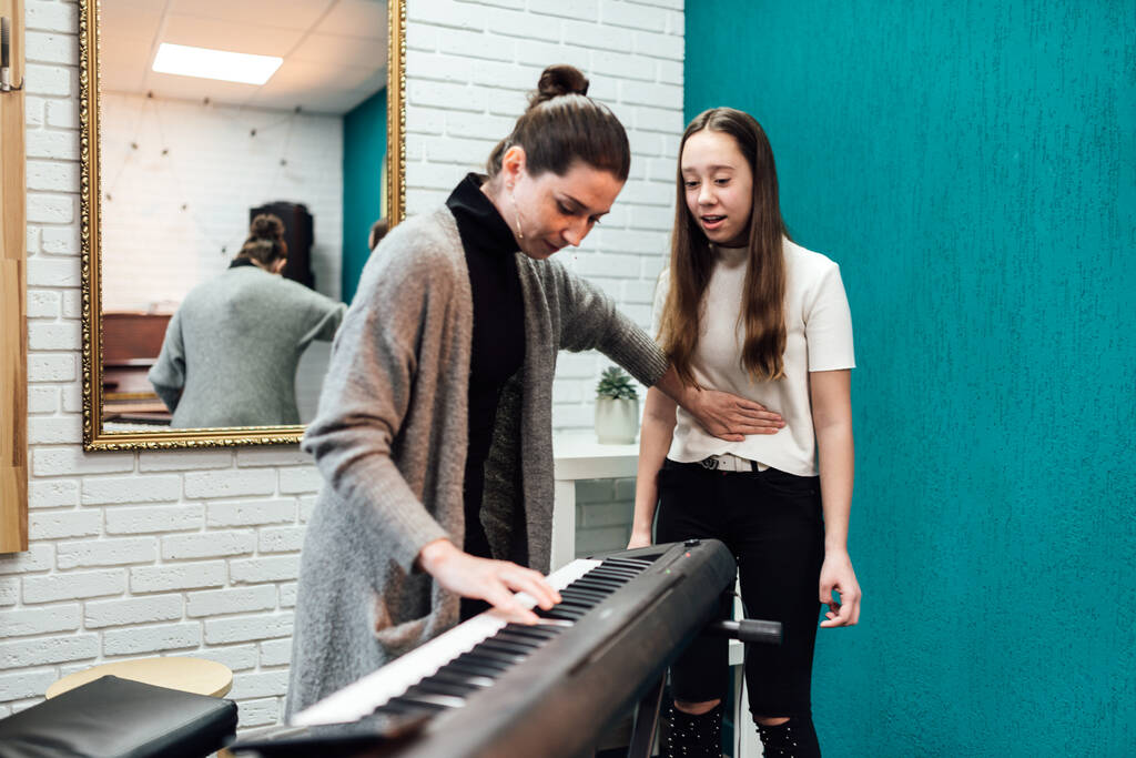 Mulher ensinando seu aluno a cantar enquanto acompanha no piano eletrônico - Foto, Imagem