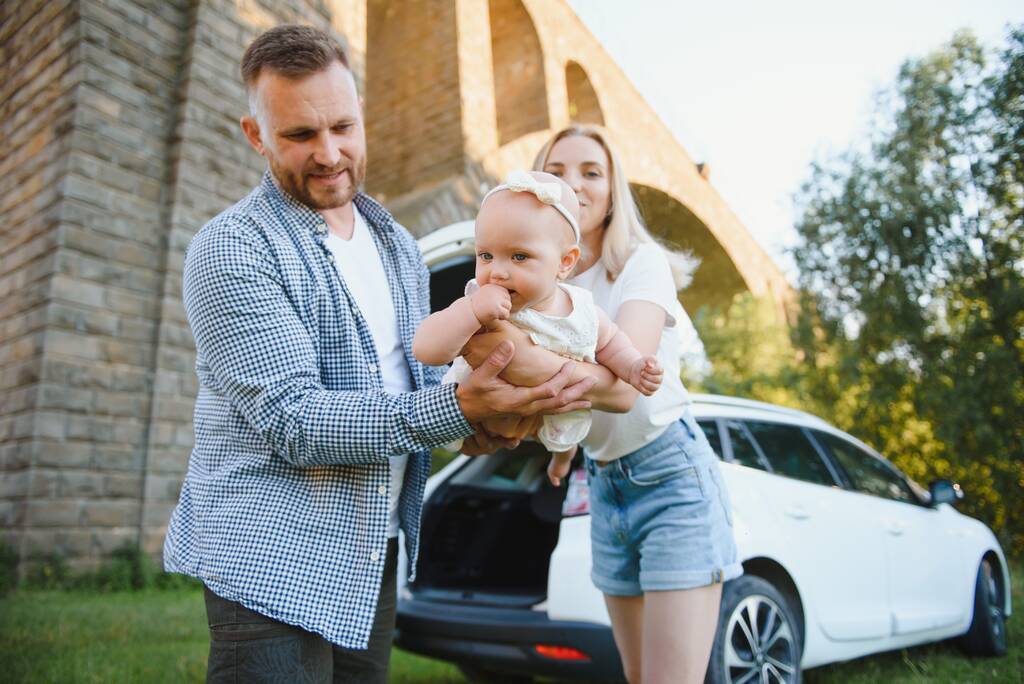 Familia joven tres personas en ropa blanca tienen picnic. Hermosos padres e hija viajan en coche durante las vacaciones de verano. Escena en el parque - Foto, imagen
