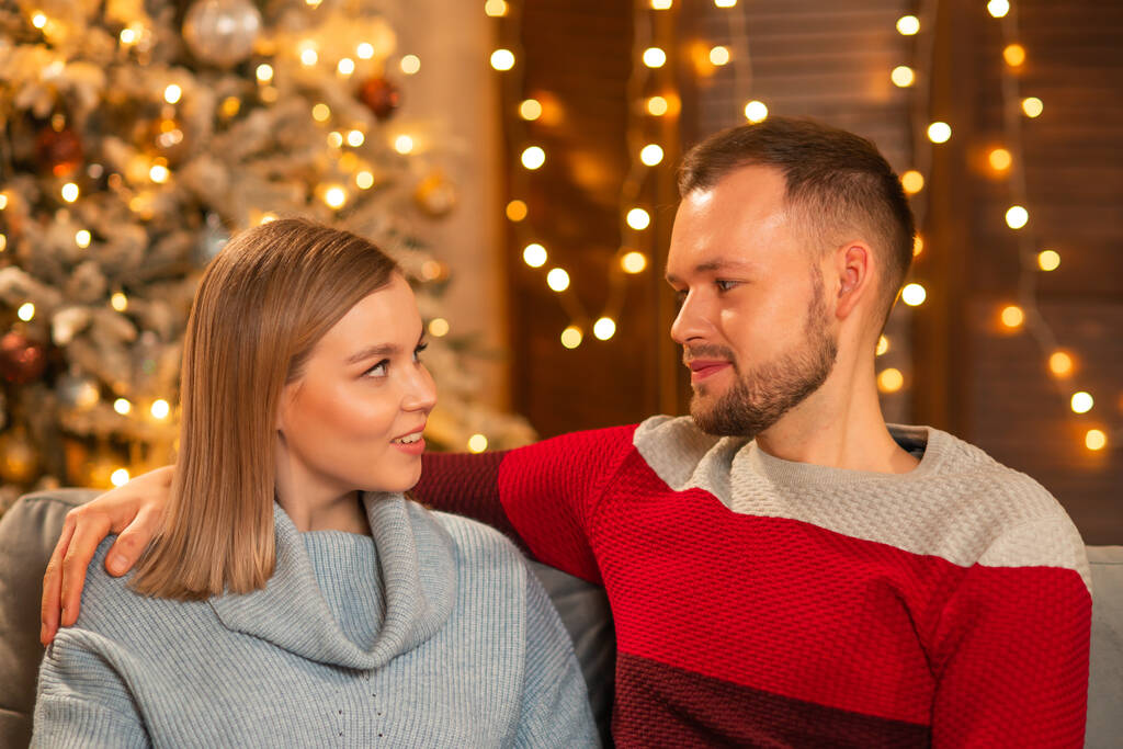 Young loving couple celebrating Christmas at home. Young man and his attractive girlfriend in a home interior with a Christmas tree. - Photo, Image