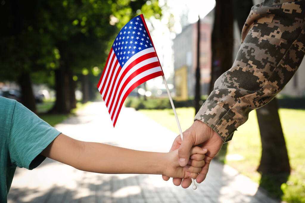 Voják a jeho malý syn s americkou vlajkou, držící se venku za ruce, zblízka. Den veteránů v USA - Fotografie, Obrázek